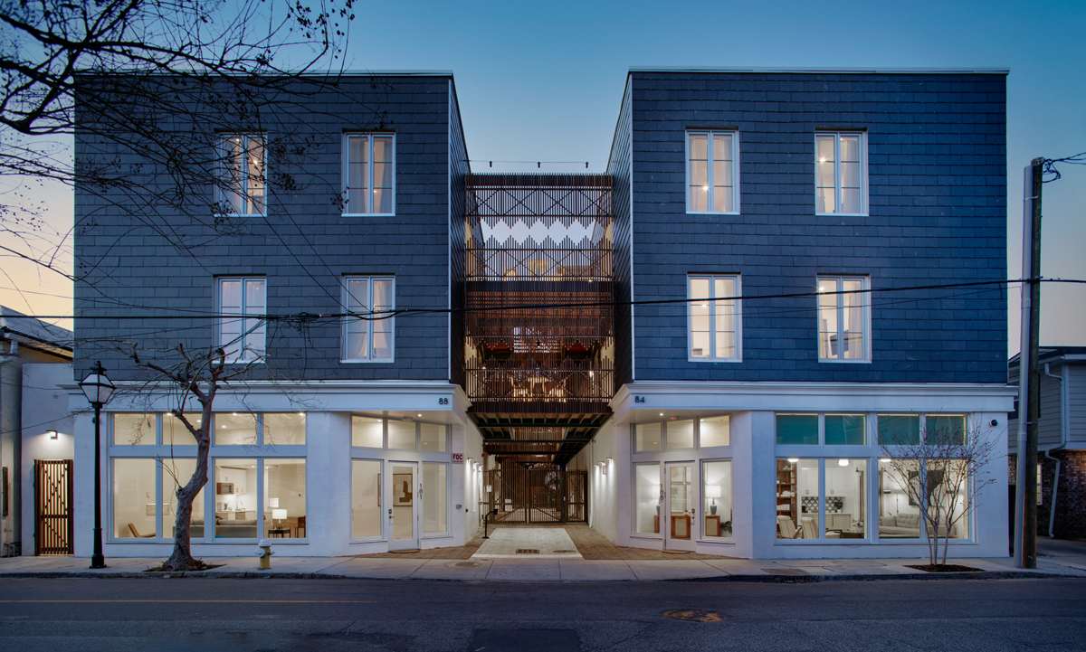 A three-story building with a blue-gray exterior and white trim, featuring a central courtyard and lit windows.