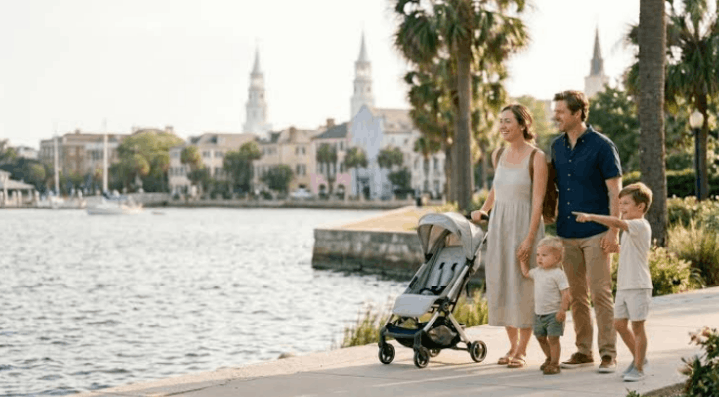 A happy family with a stroller walks along the waterfront battery park while on a trip to visit Charleston SC with kids.