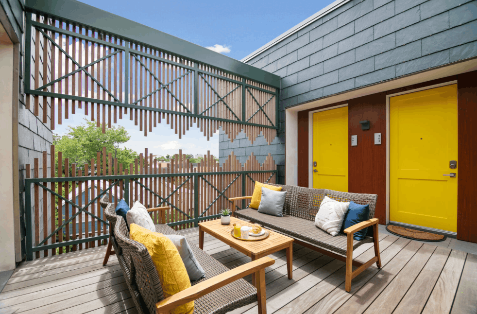 A modern outdoor patio deck with two bright yellow doors, wicker sofas, and a wooden privacy screen