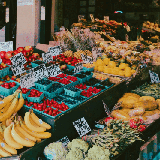 Colorful fruit and vegetable market stall displaying a variety of fresh produce with visible price tags.