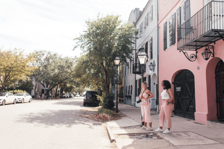 Visitors standing on the sidewalk next to the iconic rainbow row buildings  on a sunny day in Charleston, SC.