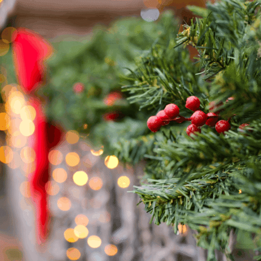 Close-up of a Christmas garland with red berries and glowing bokeh lights for a festive atmosphere