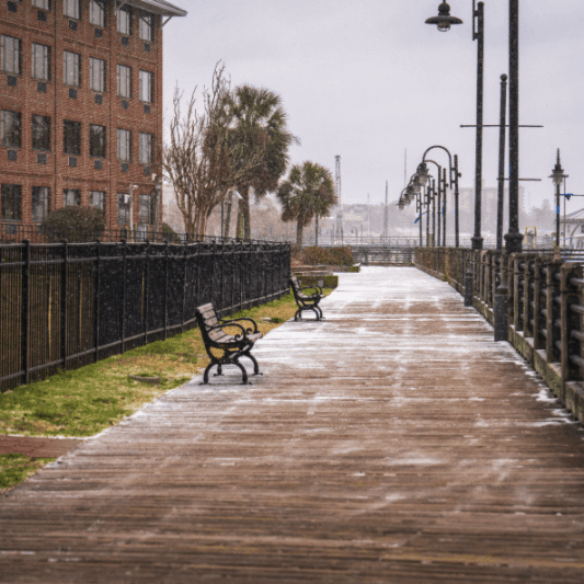 Scenic winter view of a waterfront boardwalk lightly dusted with snow and lined with empty benches.