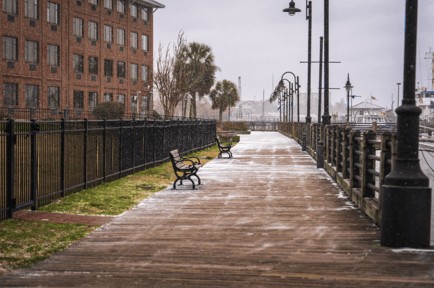 Scenic winter view of a waterfront boardwalk lightly dusted with snow and lined with empty benches.